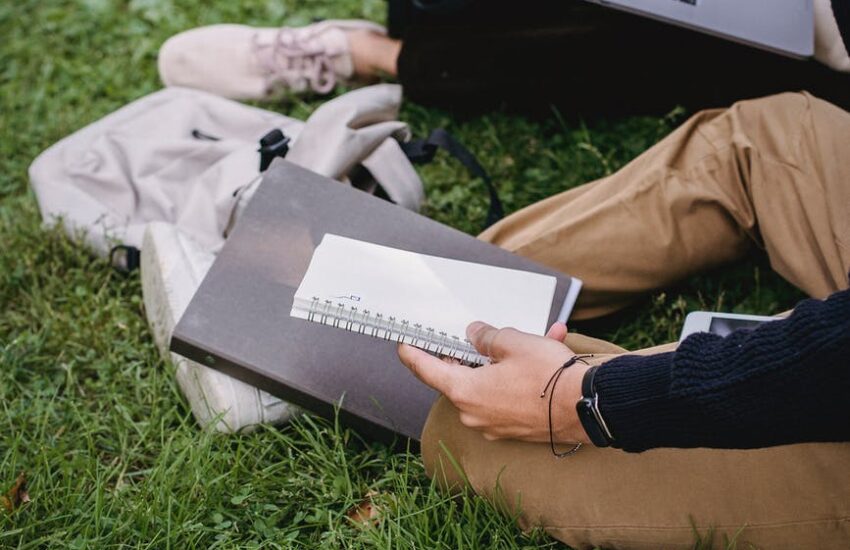 crop unrecognizable students studying together on grassy meadow