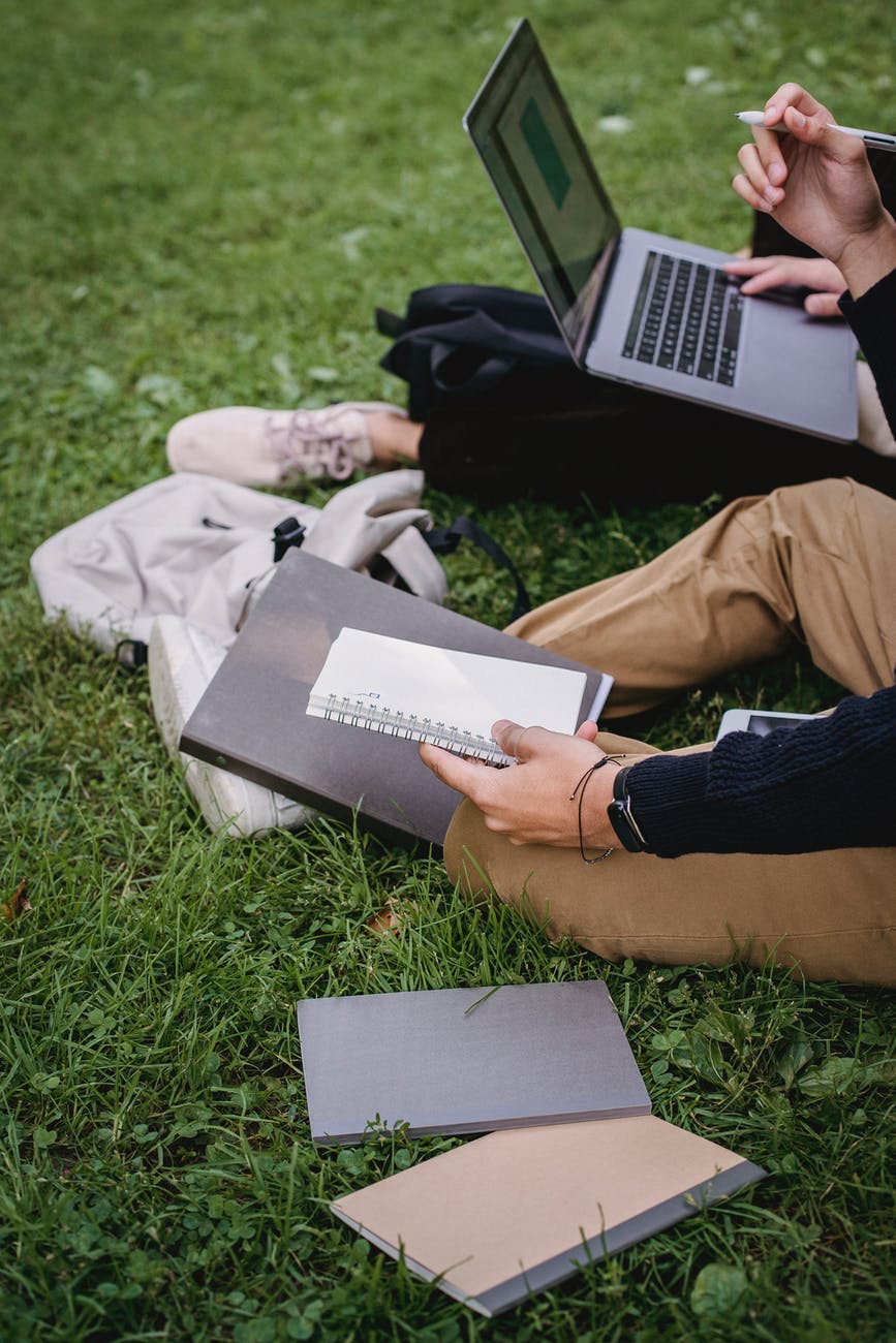 crop unrecognizable students studying together on grassy meadow