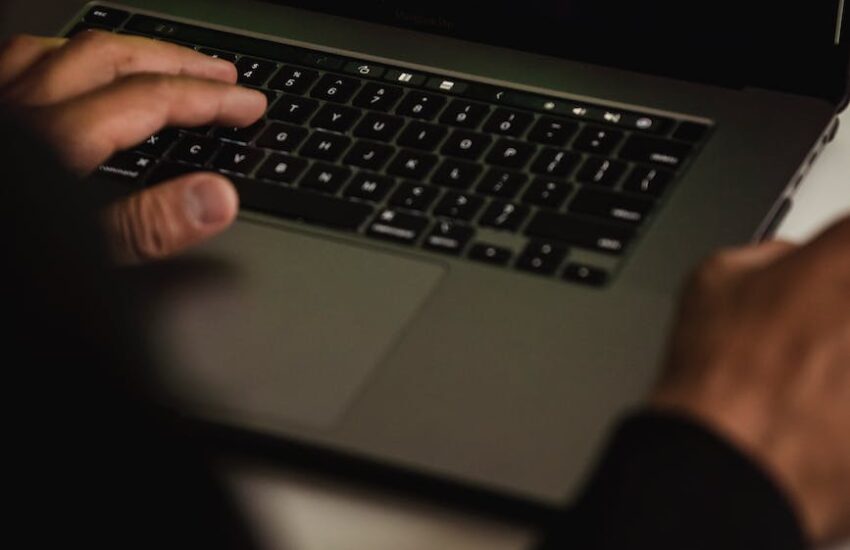 crop hacker typing on laptop with data on screen